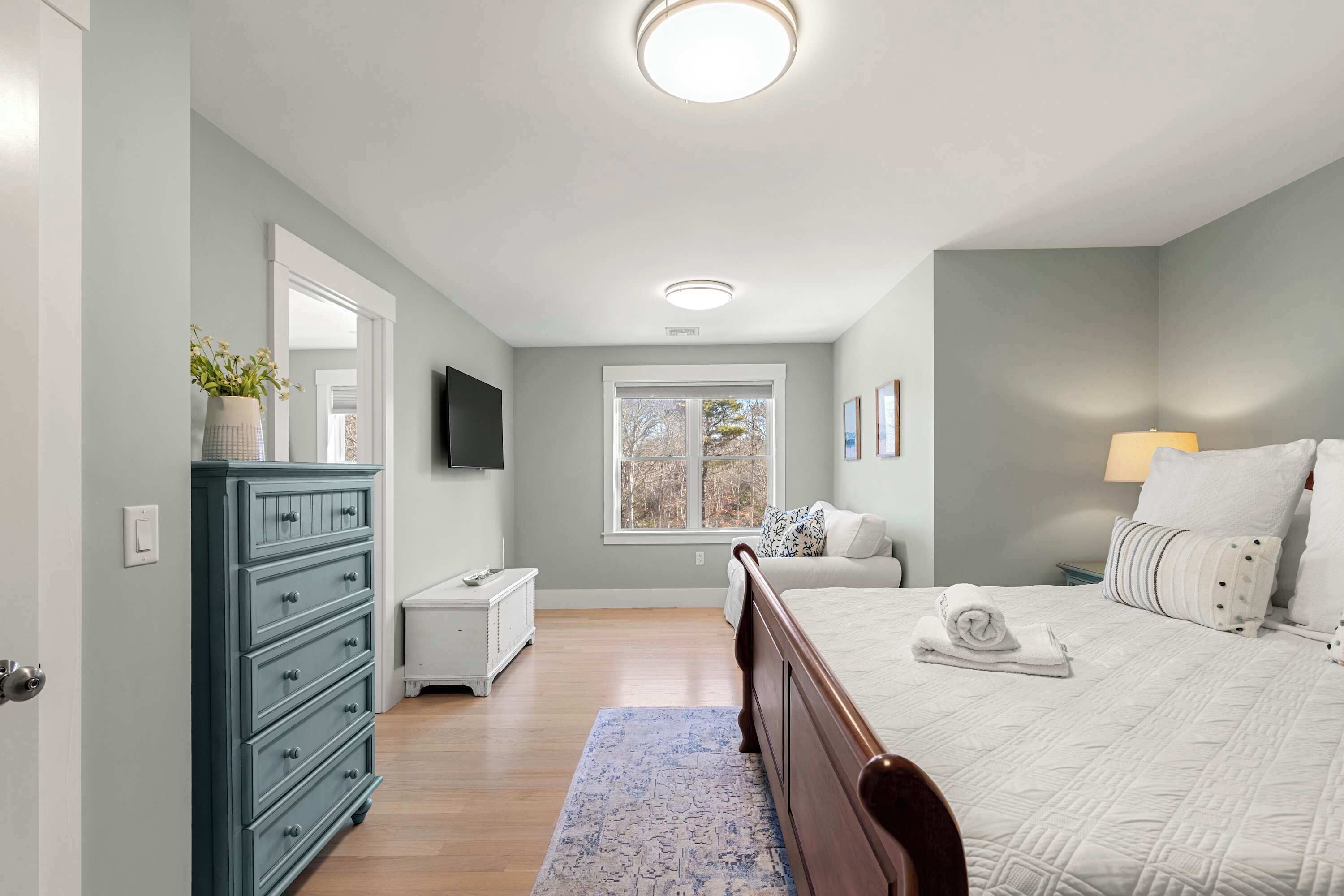 A bedroom with a bed, dresser, TV, window, and a lamp.