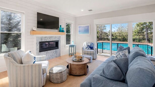A living room with a fireplace, a pool, and a large window. - Upscale Beach Retreat w Pool, Half Mile to Beach! (Dennis)