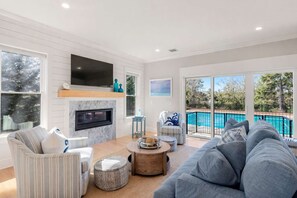 A living room with a fireplace, a pool, and a large window. - Upscale Beach Retreat w Pool, Half Mile to Beach! (Dennis)