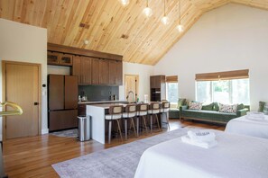 A spacious kitchen with wooden cabinets and a central island, a cozy living area with a sofa and a dining table, and a large window providing natural light. - Elegant Modern Retreat with Hot Tub and Game Room (Dennis)