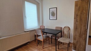 A dining area with a table and chairs, a window with blinds, a framed picture on the wall, and a wooden door. - Cozy 1 bedroom apartment in a quaint Chemnitz neighborhood (Chemnitz)