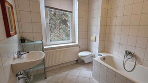 A bathroom with a sink, toilet, bathtub, and a window with a view of trees. - Cozy 1 bedroom apartment in a quaint Chemnitz neighborhood (Chemnitz)