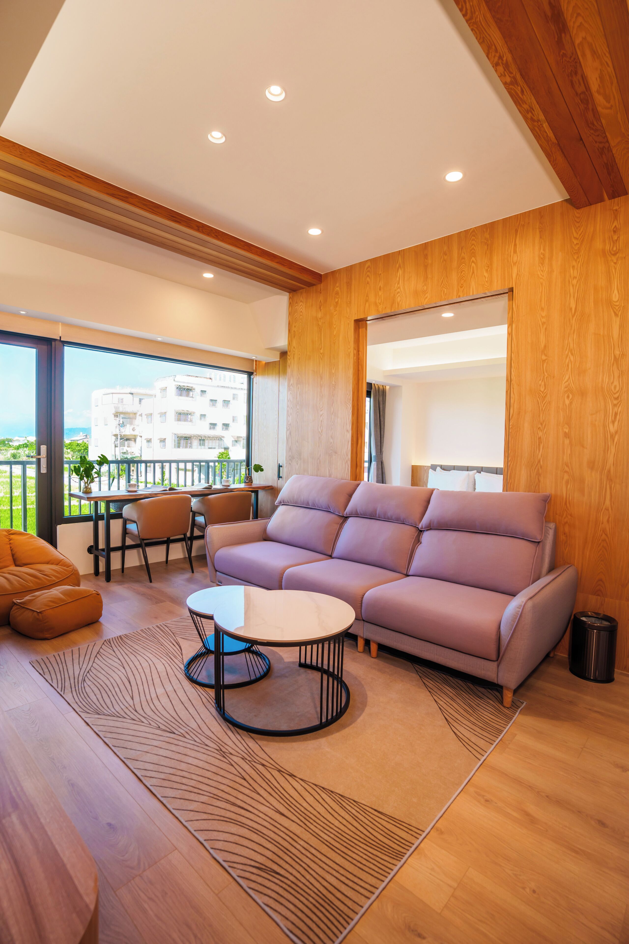Una sala de estar moderna con sofá, mesa de centro y sillones, un balcón con vistas, y paneles de madera.