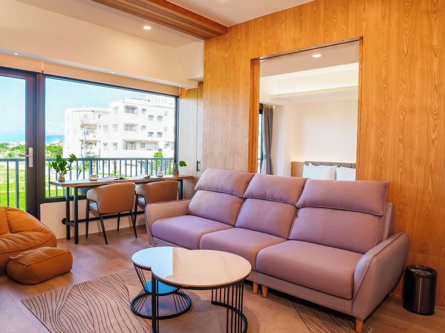 Una sala de estar moderna con sofá, mesa de centro y sillones, un balcón con vistas, y paneles de madera.