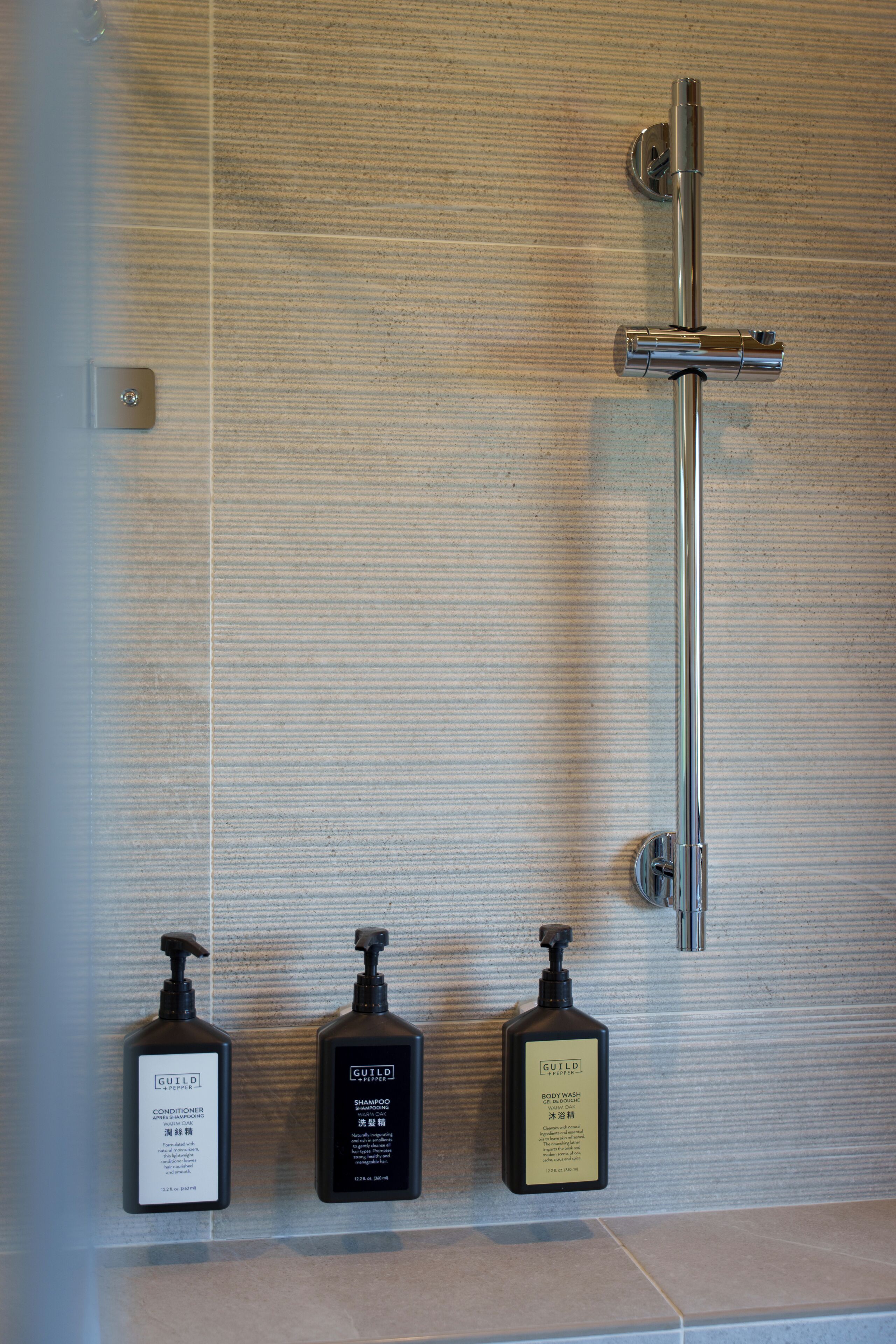 Ein Badezimmer mit Dusche, drei Shampoo-Flaschen und Toilette.