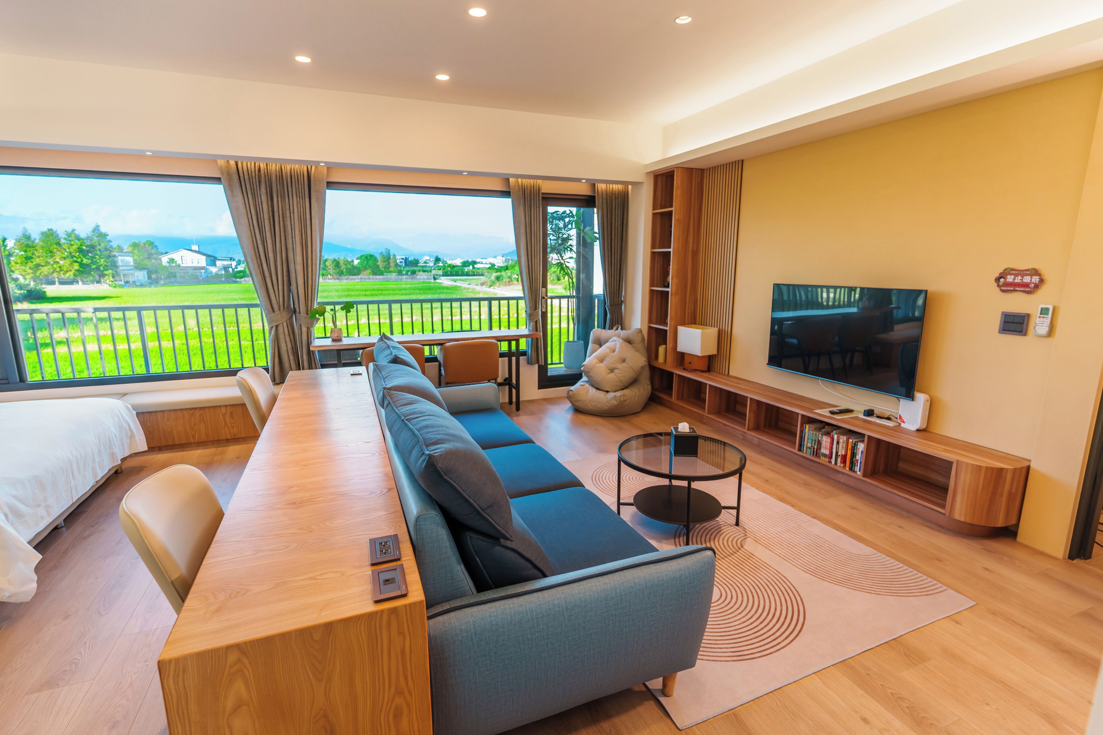 A modern living room with a large sofa, a TV, and a balcony with a view of the landscape.