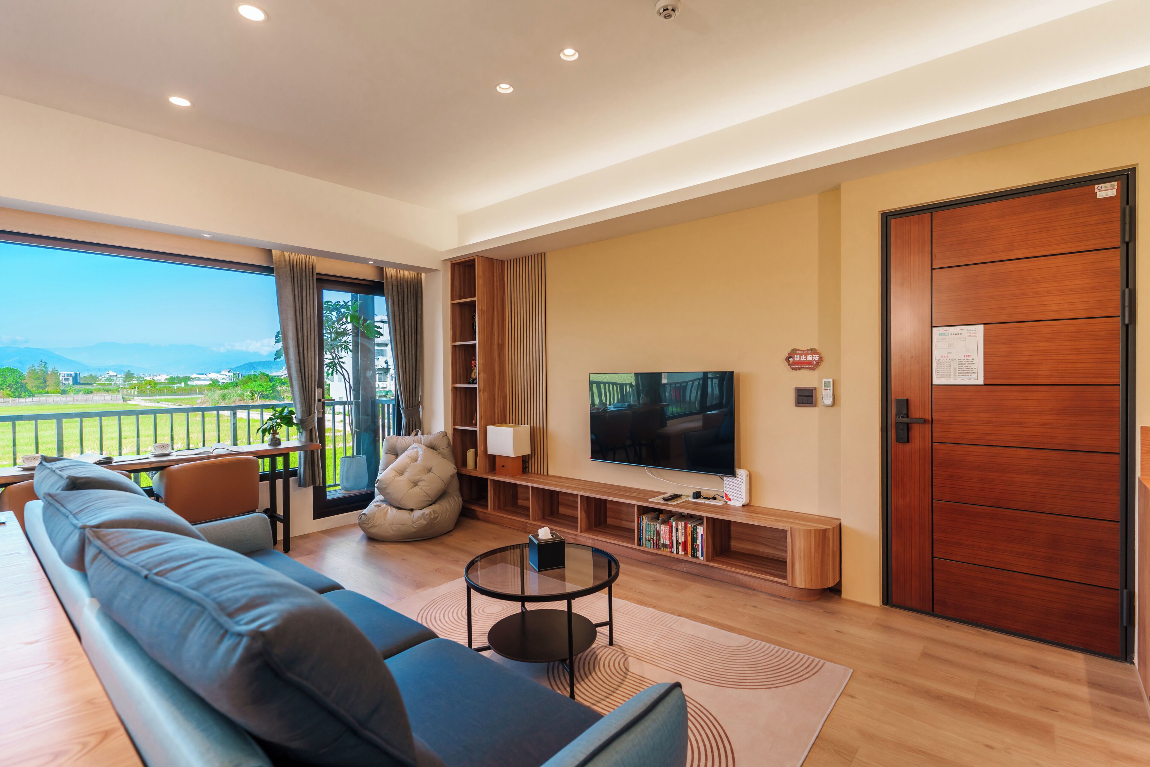 Ein modernes Wohnzimmer mit Sofa, Fernseher und einem Balkon mit Landschaftsblick.