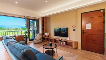 Ein modernes Wohnzimmer mit Sofa, Fernseher und einem Balkon mit Landschaftsblick.