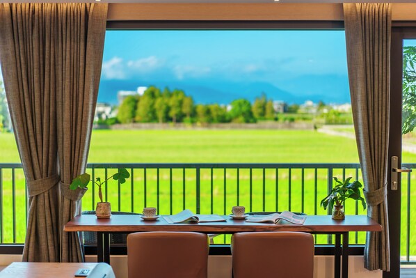 A room with a view of a green field and mountains, a table with a plant, and two chairs. - Yosemite No.2 (Yilan)
