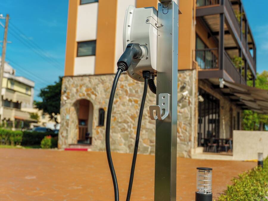 An electric vehicle charging station mounted on a metal pole with a building in the background.