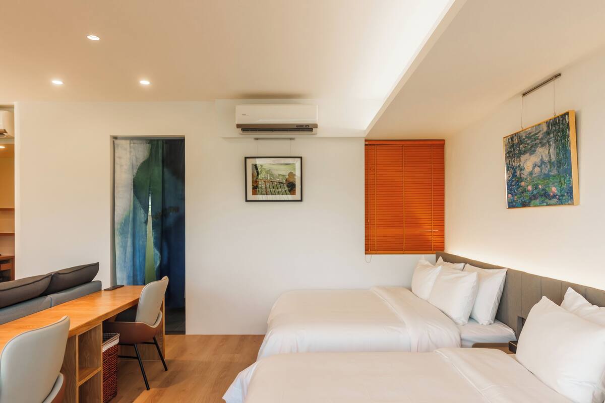 A modern hotel room with two beds, a desk, and a chair.