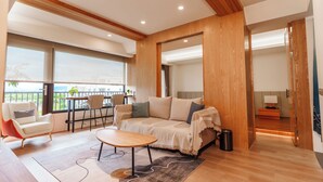 Een moderne woonkamer met een bank, salontafel en stoelen, een balkon met uitzicht, en houten lambrisering.