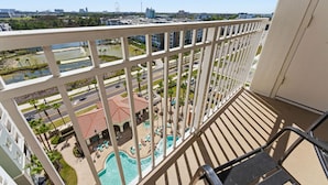 A balcony with a view of a swimming pool, palm trees, and distant buildings. - Family 2-bedroom Suite in Prime Orlando Location (Orlando)