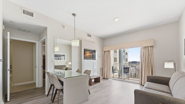 A modern hotel room with a dining area, a sofa, a large window with curtains, and a balcony. - Family 2-bedroom Suite in Prime Orlando Location (Orlando)