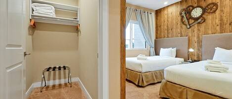 A hotel room with two beds, a wooden wall clock, a window with curtains, and a small radiator.