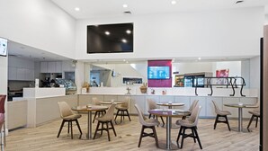 Un restaurante moderno con mesas y sillas redondas, una zona de cocina y un televisor de pantalla plana grande montado en la pared.
