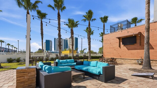 Un patio al aire libre con mobiliario de mimbre, palmeras y un paisaje urbano de fondo.
