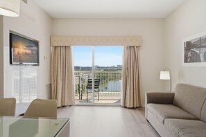 A hotel room with a balcony, a TV, a sofa, a glass table, and a lamp. - Comfortable 1-bedroom apt in Prime Orlando Spot (Orlando)