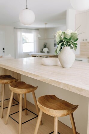 Eine Küche mit heller Arbeitsplatte, Holzstühlen und einer weißen Vase mit Blumen.