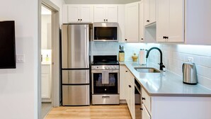 Une cuisine moderne dotée d’appareils électroménagers en acier inoxydable, de meubles blancs et d’un plancher en bois.