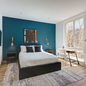 Ein modernes Schlafzimmer mit einem Bett, Nachttischen, einem Schreibtisch und einem großen Fenster.