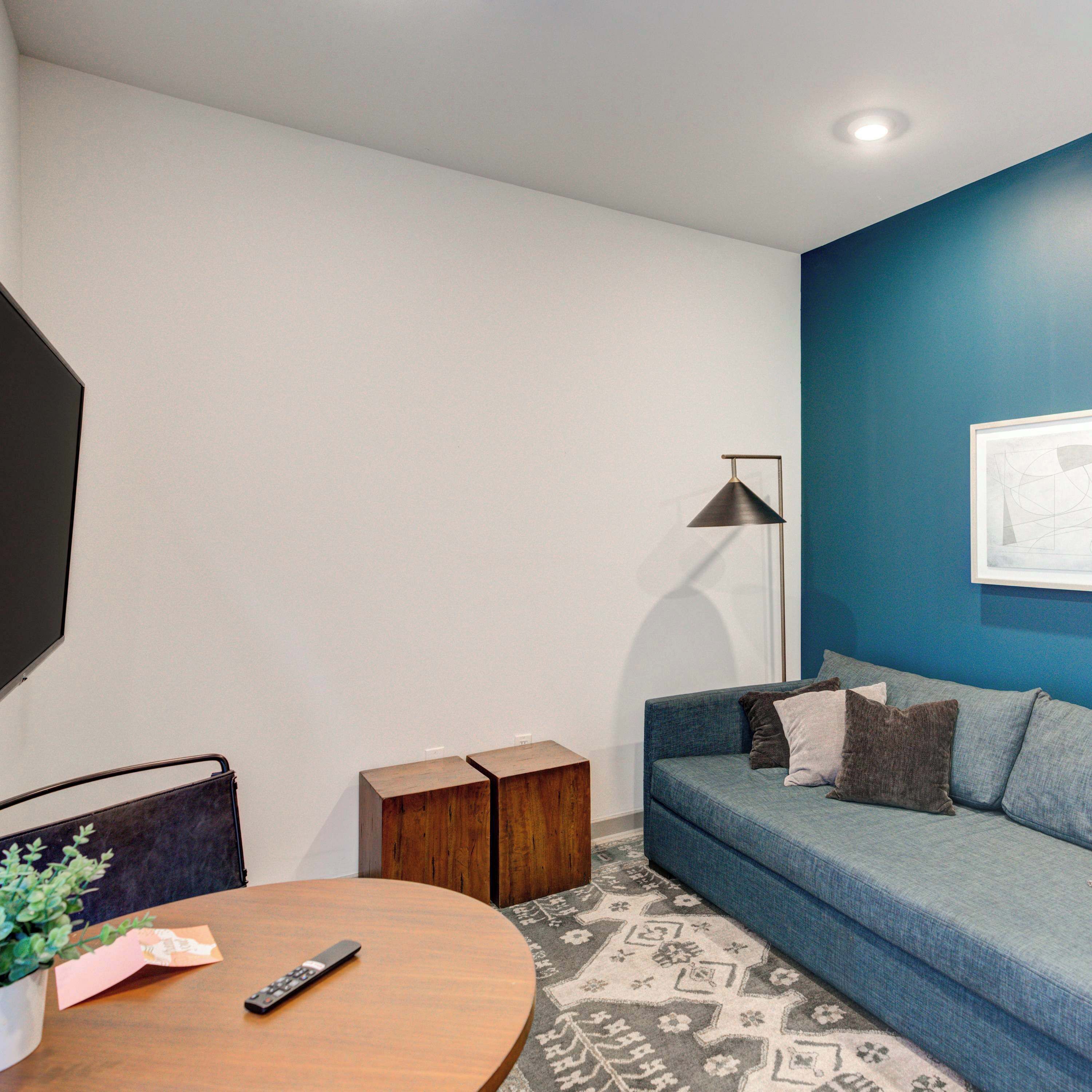 Una sala de estar moderna con una pared azul de acento, un sofá, una mesa de centro, una lámpara de pie y un televisor.