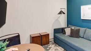 A modern living room with a blue accent wall, a sofa, a coffee table, a floor lamp, and a television. - Prime Ludlow Studio | Steps from UPenn & CHOP (Philadelphia)