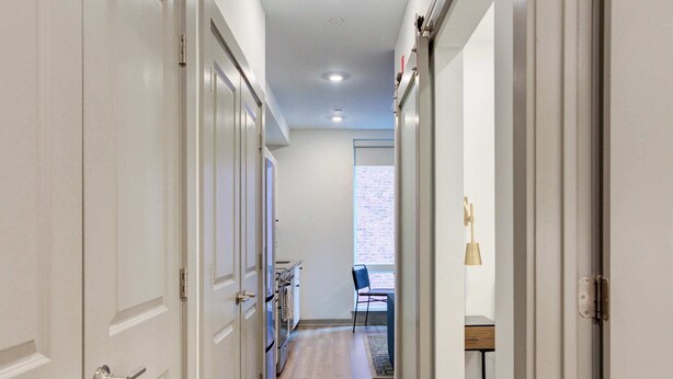 A hallway with white doors, a kitchen area with a blue chair, and a window with a brick wall view. - Prime Ludlow Studio | Steps from UPenn & CHOP (Philadelphia)