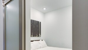 A bedroom with a bed, a wooden floor, and a white wall with a black abstract painting. - Prime Ludlow Studio | Steps from UPenn & CHOP (Philadelphia)