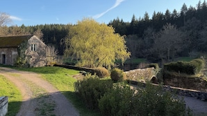 A stone building with a window, surrounded by greenery and a stone bridge. - Former mill of the Château de Bourbilly transformed into a pretty country house (Vic-de-Chassenay)