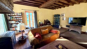 A cozy living room with a wooden ceiling, a sofa, a television, a bookshelf, and a cabinet. - Former mill of the Château de Bourbilly transformed into a pretty country house (Vic-de-Chassenay)