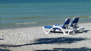 Deux chaises de plage sur une plage de sable, avec une eau bleu clair en arrière-plan.