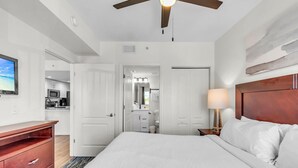 A hotel room with a bed, a desk, a lamp, a ceiling fan, and a view of the kitchen. - Sunset Vistas 302n (Treasure Island)