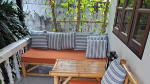 Een kamer met een zithoek met een houten bankje, een kleine tafel en een raam met uitzicht op groen.