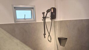 Een badkamer met een douche, toilet, wastafel en een klein raam.