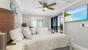 Una camera da letto con un letto, una ventola a soffitto, una TV, una finestra e un'uscita che dà su un balcone.
