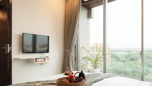 Un dormitorio con una cama, televisión, ventana con vistas, planta y una cesta con objetos.