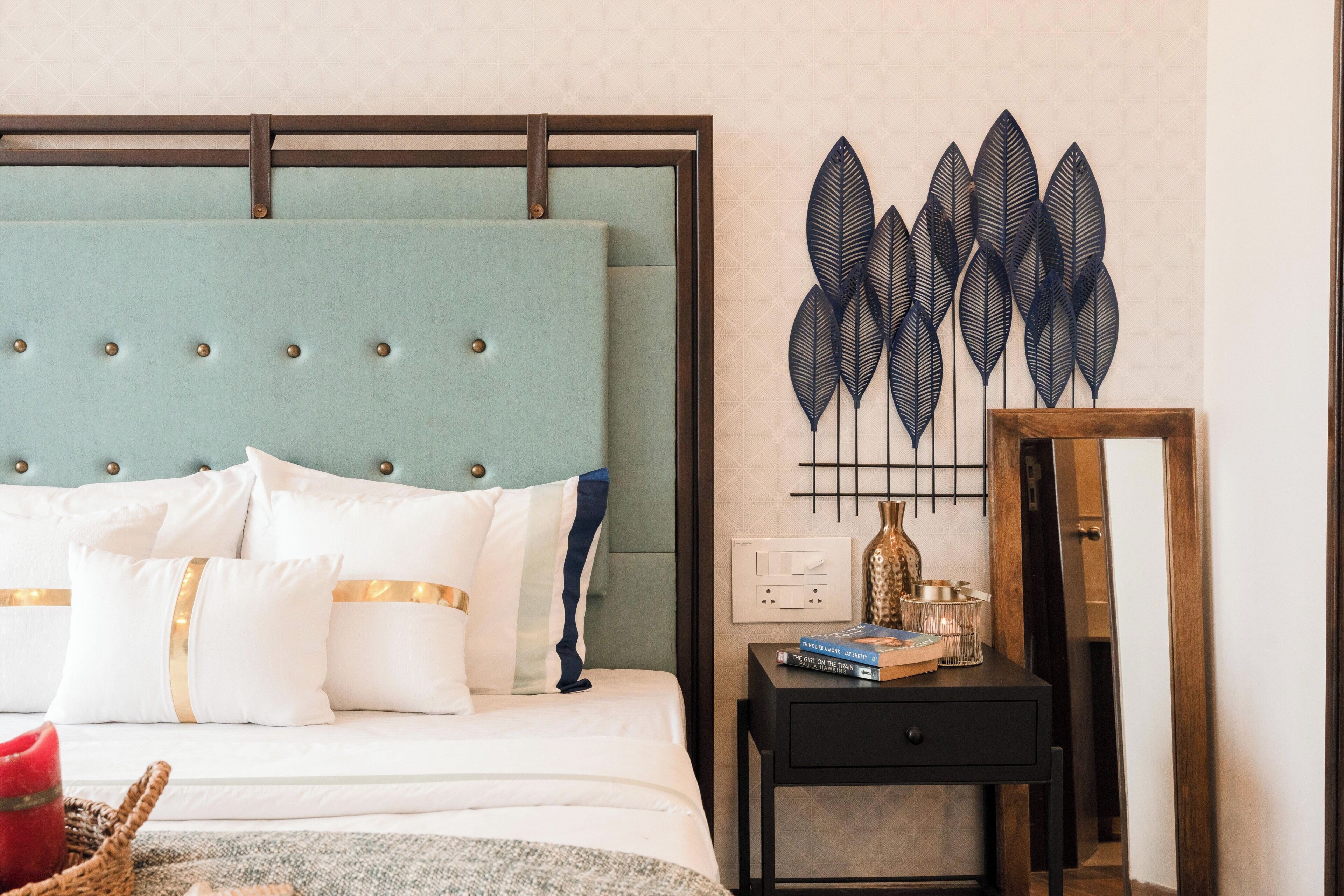 A neatly made bed with a tufted headboard, a bedside table with a mirror, and decorative wall art.