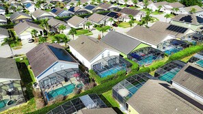 A residential area with multiple houses, some with solar panels, and a large swimming pool with a glass enclosure. - 6BR Pool & Spa Home Near Disney (Clermont)