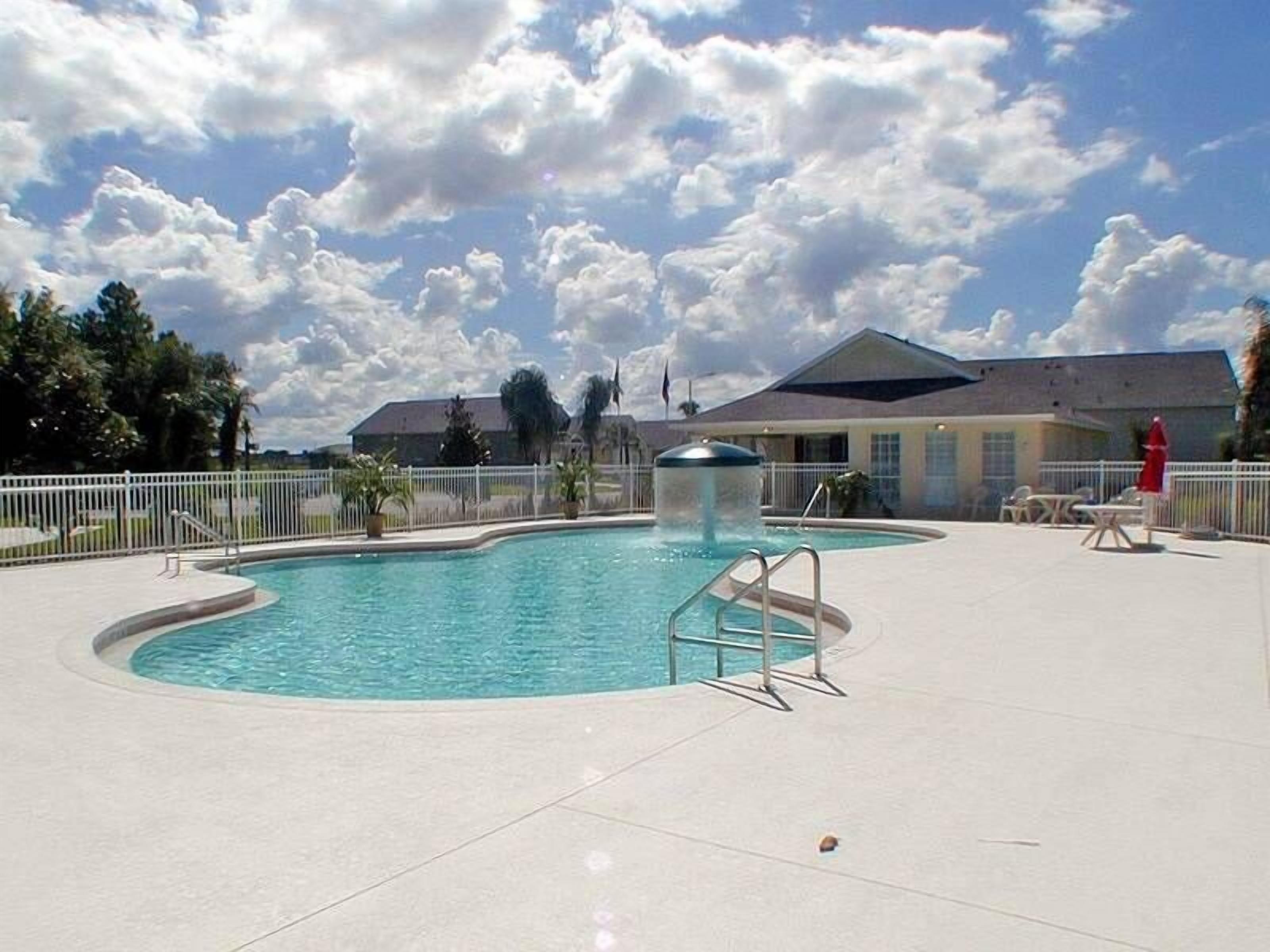Une piscine avec un plongeoir, entourée d’une clôture, et un bâtiment en arrière-plan.