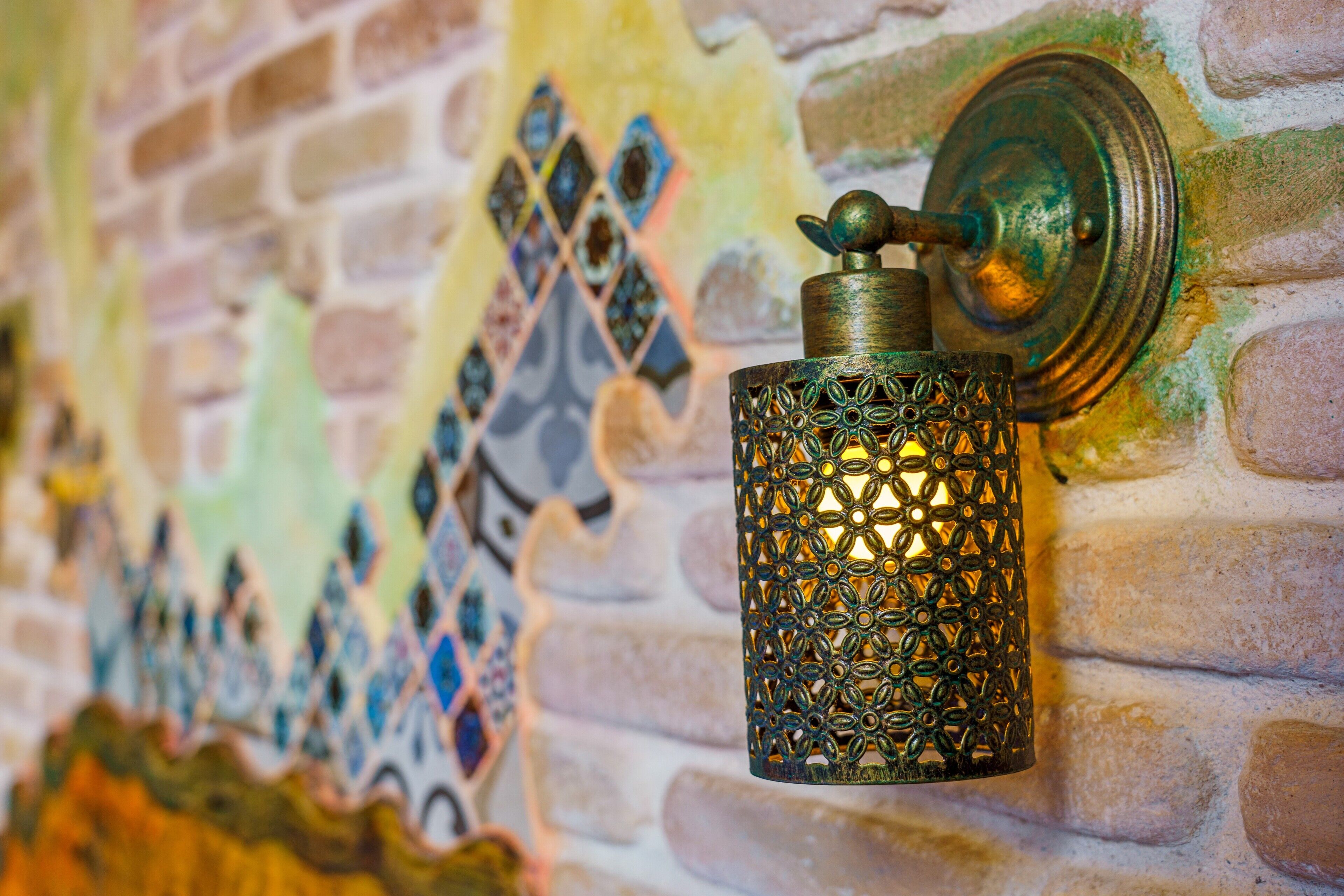A decorative metal lantern attached to a brick wall with mosaic tiles.