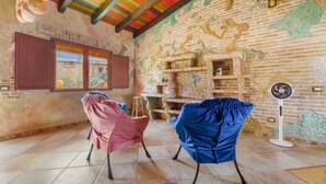 A room with a brick wall, a fan, and two chairs. - Room 'BATTLÒ' with Mountain View, Shared Terrace and Wi-Fi (Teulada)