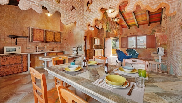 A spacious kitchen with a dining area, featuring a large wooden table, chairs, and a brick wall. - Room 'BATTLÒ' with Mountain View, Shared Terrace and Wi-Fi (Teulada)