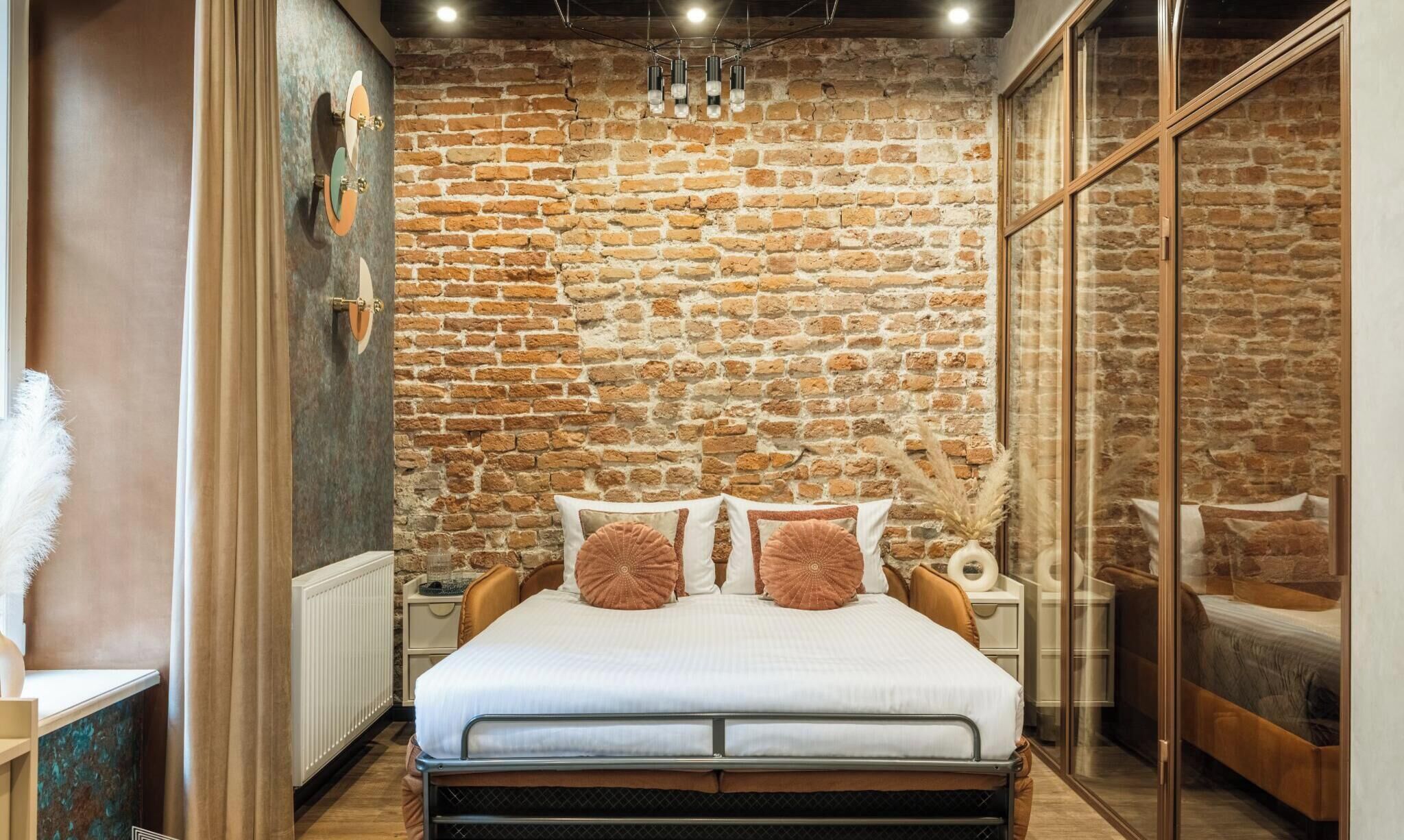 A bedroom with a brick wall, a bed with white bedding, a nightstand, and a mirror.