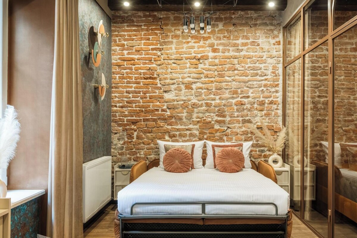 Un dormitorio con pared de ladrillo, cama con ropa de cama blanca, mesita de noche y espejo.