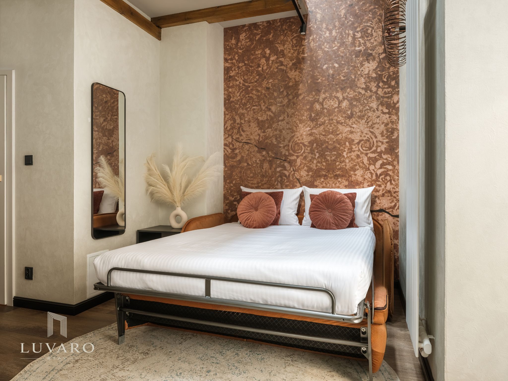 A bedroom with a bed, a nightstand, a mirror, and a wall with a textured pattern.