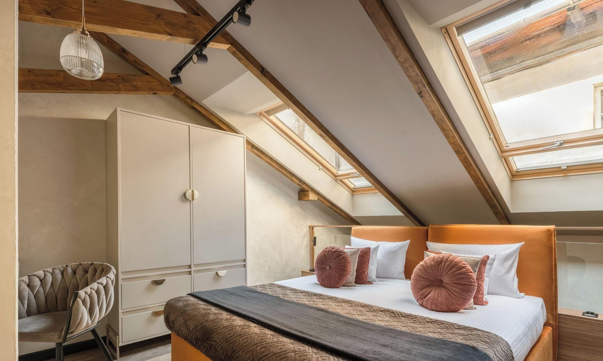 A bedroom with a sloped ceiling, a bed with a headboard, a wardrobe, a chair, and a skylight.