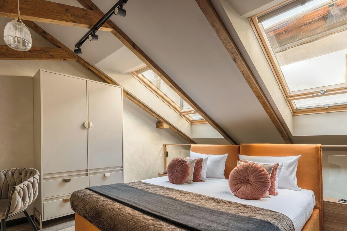 Un dormitorio con techo inclinado, una cama con cabecero, un armario, una silla y un tragaluz.