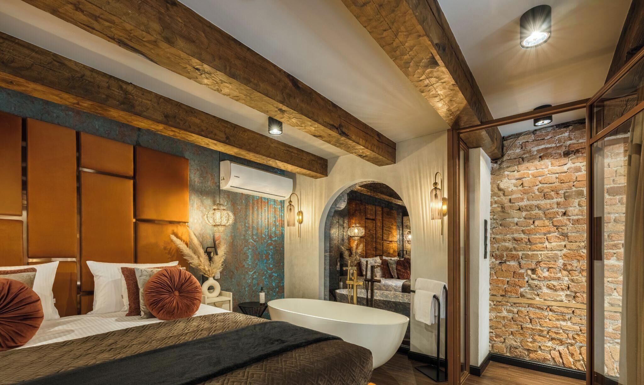 A bedroom with a large bed, a bathtub, and a stone wall.