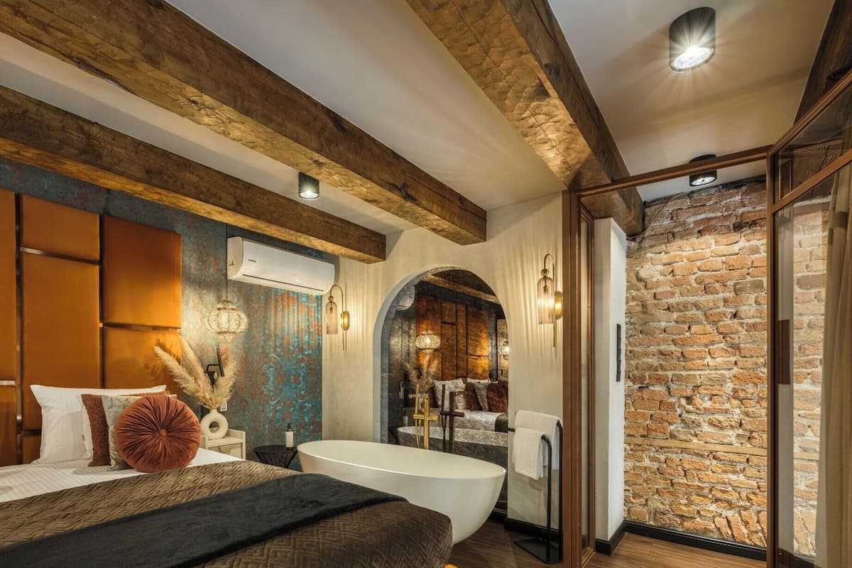 A bedroom with a large bed, a bathtub, and a stone wall.